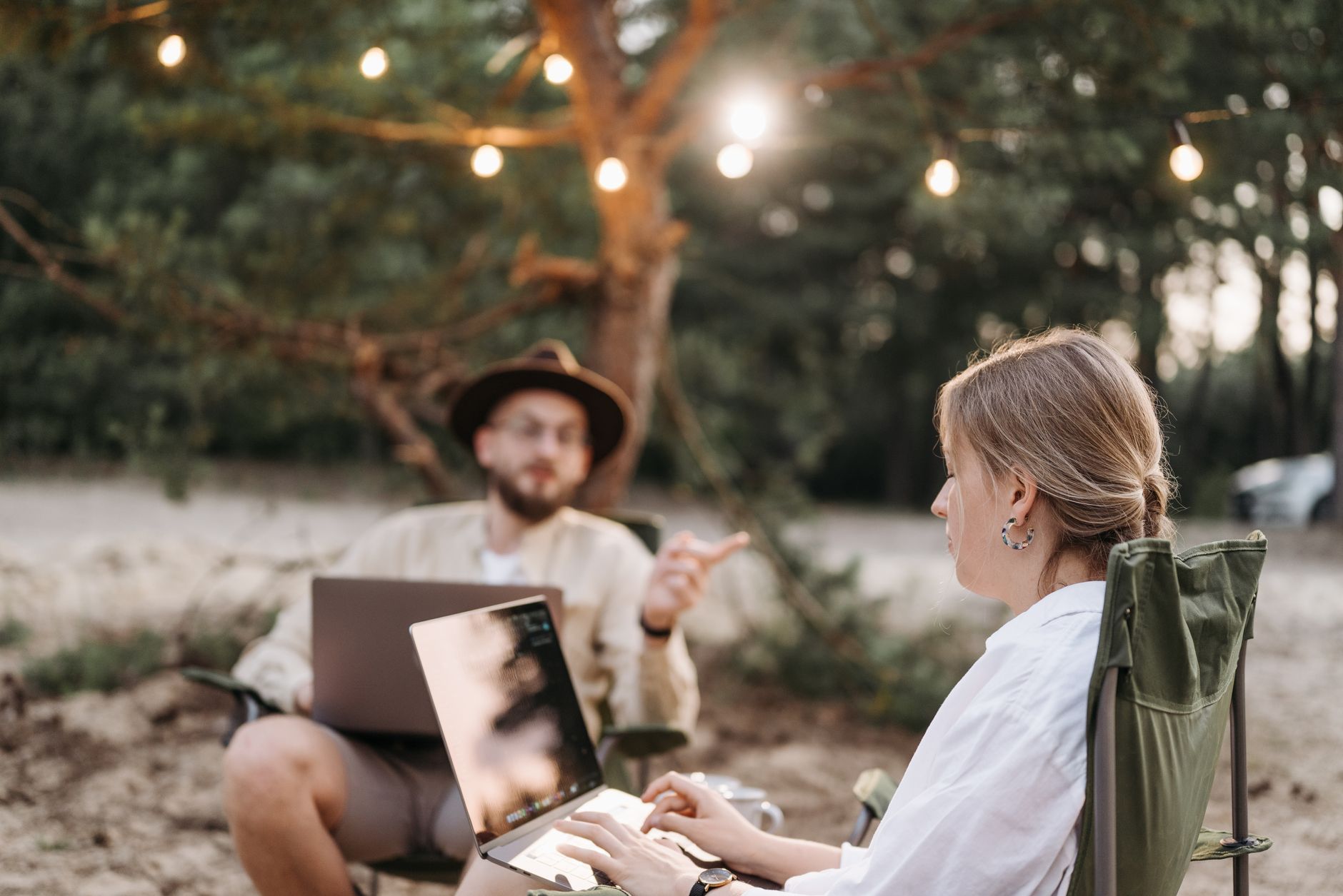 Two adults working on laptops in a rustic outdoor setting with ambient lighting.