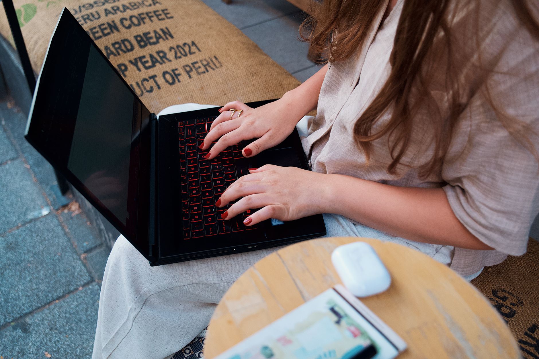 A woman with long hair typing on a laptop outdoors at a café, focusing on remote work.
